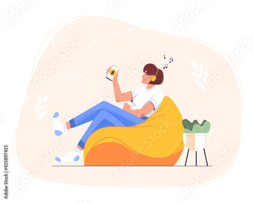 Flat happy teen girl in headphones sitting at home in bean bag chair and using smartphone for online education. Woman relaxing and listening to music, audio podcast, radio or audiobook on mobile phone