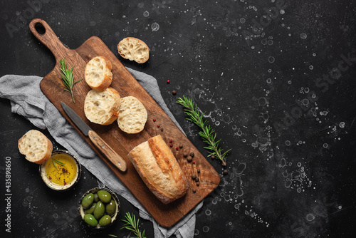 Fresh Italian ciabatta bread with olive oil, olives and rosemary on a black stone background. Top view, flat lay