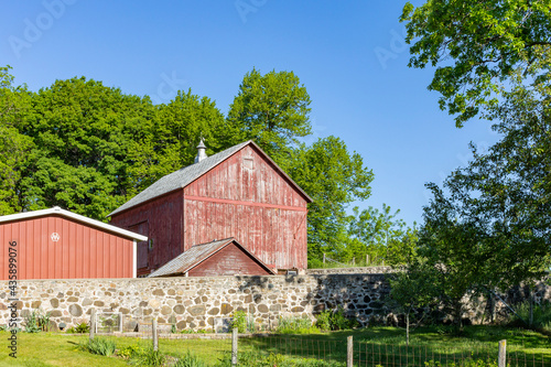 Fotografi A small faded red barn with a milk house, shed, and stone barnyard wall on a clear sunny day