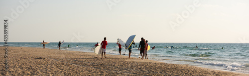 Surf school. Group of young guys and girls on the beach and in the water learning to surf. 
