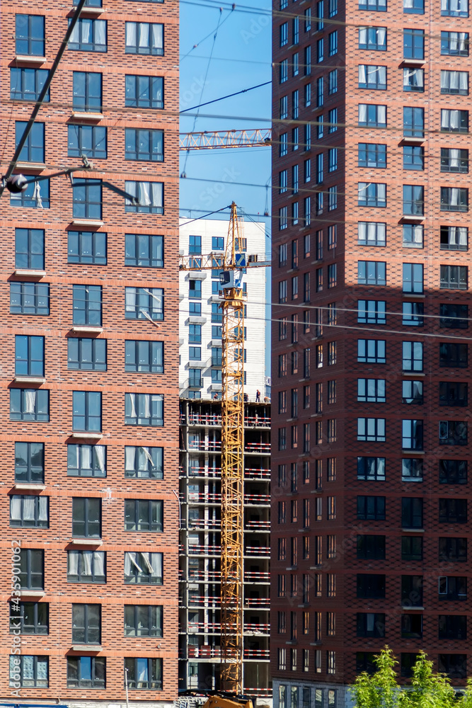 Construction crane and unfinished residential buildings against clear blue sky. Housing construction, apartment block with scaffolding