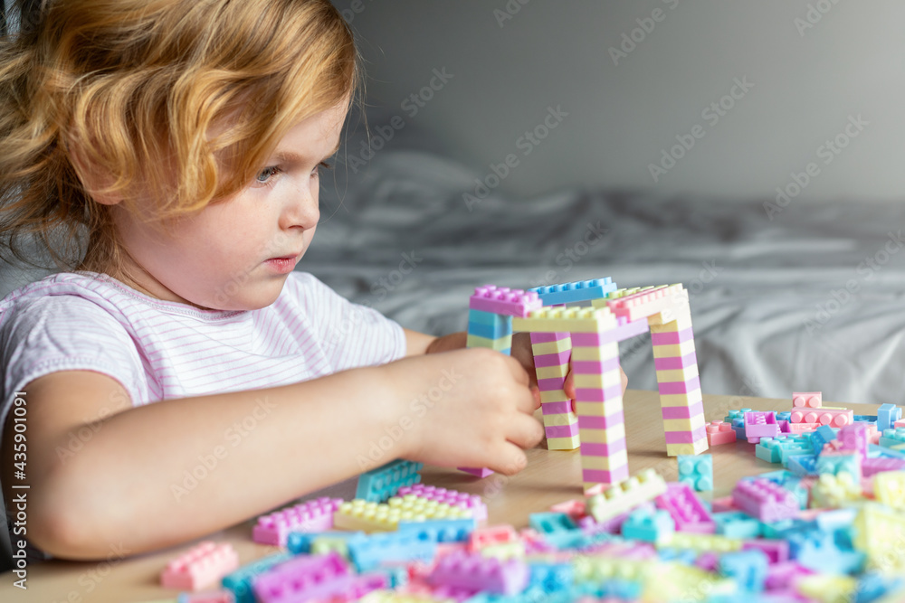Small cute preschooler girl playing with colorful toy building blocks, sitting at the table. Small cute preschooler girl playing with colorful toy building blocks, sitting at the table.
