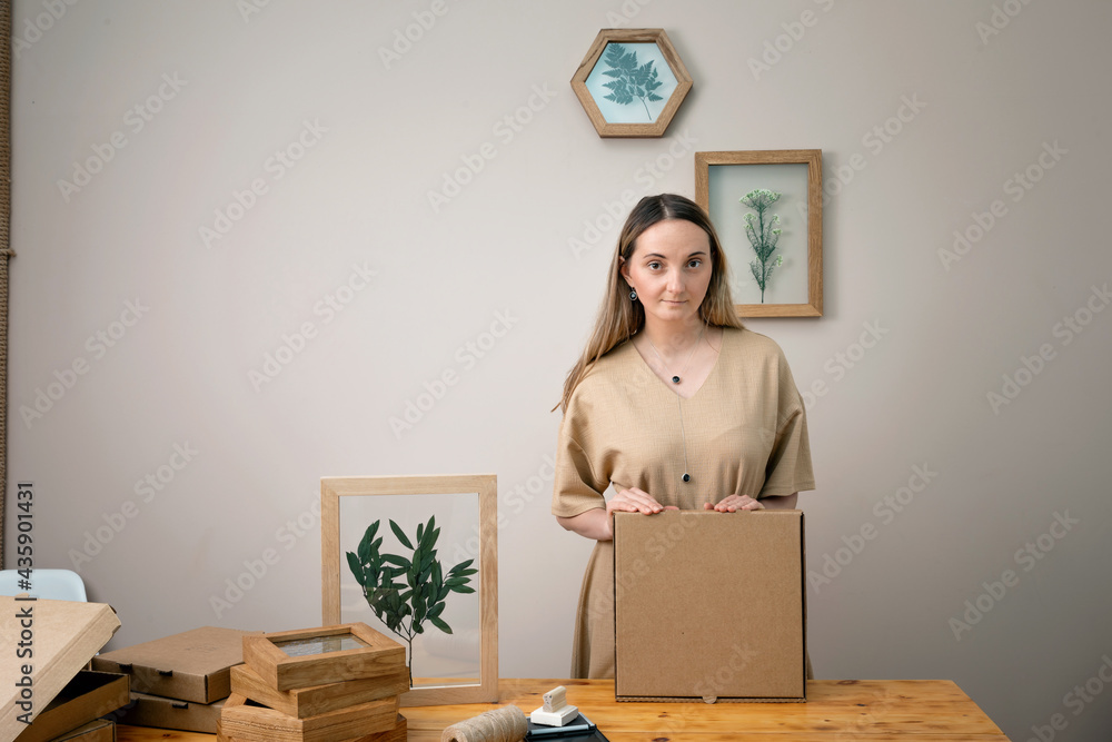 Fototapeta premium woman decorates Dry flowers in a frame. walls with botanical leaves. Eco-friendly boho decor. Real people personal space. 