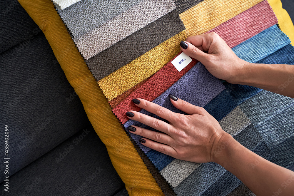 Choosing upholstery fabric color and texture from various colorful samples in a store. Female customer hands touching textile.