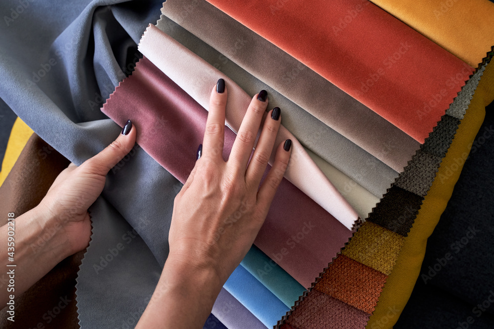 Choosing upholstery fabric color and texture from various colorful samples in a store. Female customer hands touching textile.