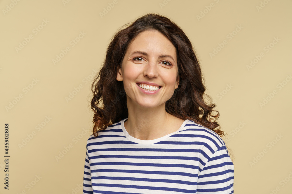 Portrait of curly caucasian female, closeup studio shot over beige background. Millennial woman with happy toothy smile and clean skin dressed in stripped t-shirt. Natural beauty and no makeup concept Portrait of curly caucasian female, closeup studio shot over beige background. Millennial woman with happy toothy smile and clean skin dressed in stripped t-shirt. Natural beauty and no makeup concept