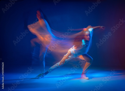 Fototapeta Naklejka Na Ścianę i Meble -  Mixed race female dancing in colorful neon light. Studio photo with long exposure. Expressive contemporary hip hop dance