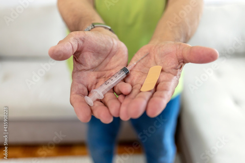 Portrait of a mature male holding a syringe with Covid-19 vaccine and plaster isolated on the white background. Cropped shot of a senior man holding syringe and adhesive bandage in hands. Copy space.