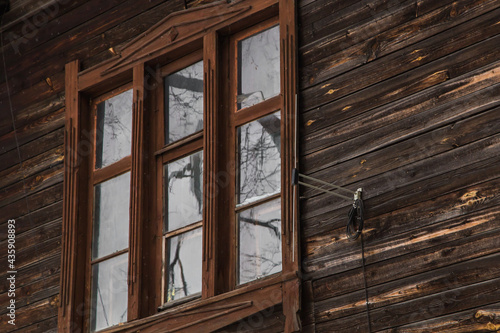 A wooden window in an old planked building with an antenna on the wall. An old wooden building in the city or countryside. Facade of a dilapidated house. Daylight.