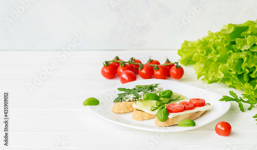 Three bruschetta on a white plate with cheese, cherry tomatoes, cucumber, arugula and basil. Copy space for text.