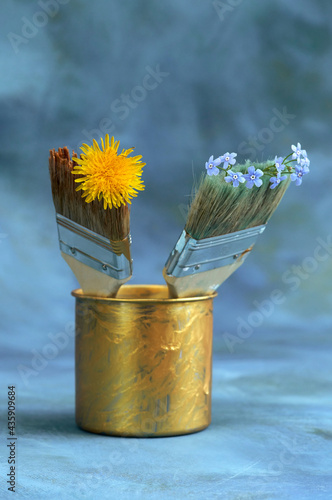 A jar with two fluted brushes  in the bristles of which are flowers  on a blue background. Selective focus.