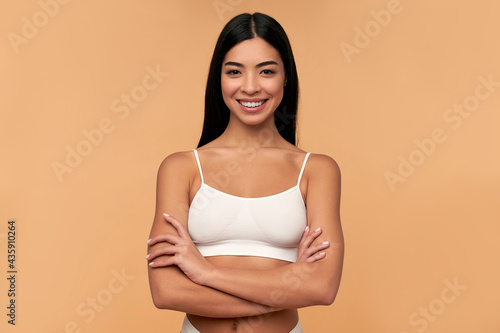 Young Asian woman in white lingerie crossed her arms on a beige background. Sports, healthy lifestyle. Spa body care. Plastic surgery. Cosmetology concept.