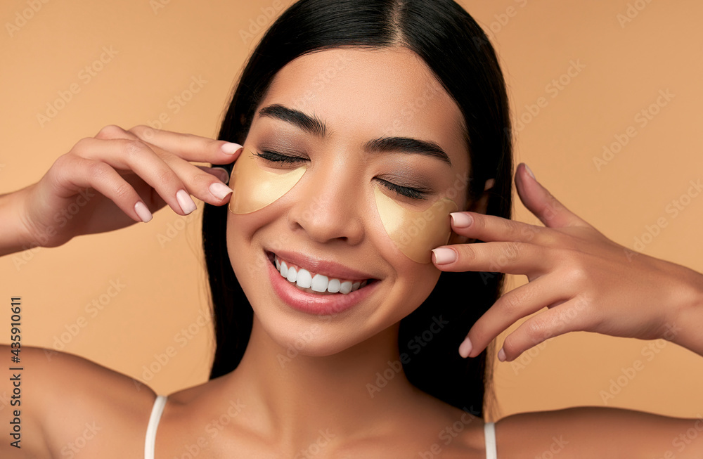 Young Asian woman in white lingerie and clean radiant skin with moisturizing patches under the eyes on a beige background. Spa care, cosmetology. Young Asian woman in white lingerie and clean radiant skin with moisturizing patches under the eyes on a beige background. Spa care, cosmetology.