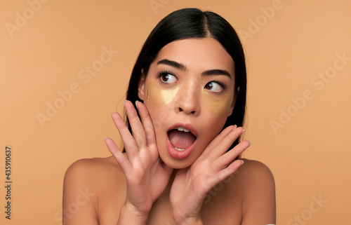 Fotografie, Obraz Young Asian woman in white lingerie and clean radiant skin with moisturizing patches under the eyes on a beige background