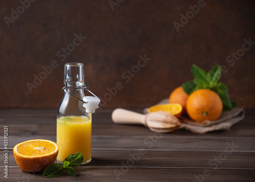 Fresh orange juice in bottle with citrus fruits and mint on a brown wooden background. Healthy and diet drink. Front view and copy space