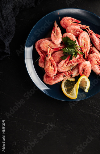 shrimp on a blue plate with lemon on a black textured background top view