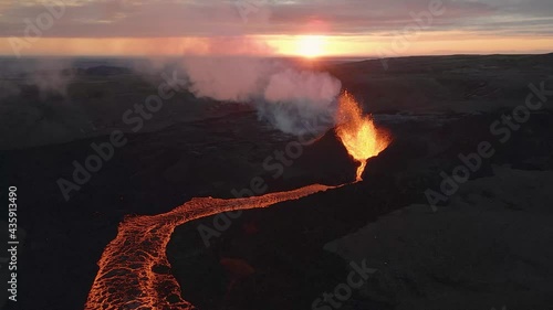 Magma spurts from crater fissure of erupting volcano with sunset in background, Iceland. Aerial forward photo