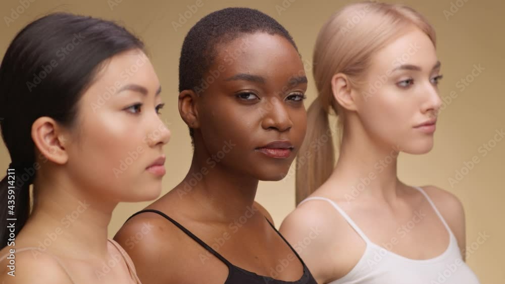 Serious young african american woman looking at camera, posing with asian and caucasian ladies friends, beige background Serious young african american woman looking at camera, posing with asian and caucasian ladies friends, beige background