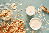 Oat milk in a glass and mug on a blue background. Flakes and ears for oatmeal and granola on a wooden plate.