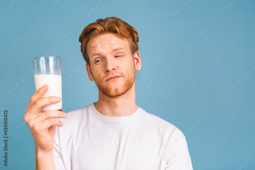 Smiling cheerful handsome young bearded man 20s wearing casual clothes posing holding in hand vegan milk isolated over blue color wall background. Smiling cheerful handsome young bearded man 20s wearing casual clothes posing holding in hand vegan milk isolated over blue color wall background.
