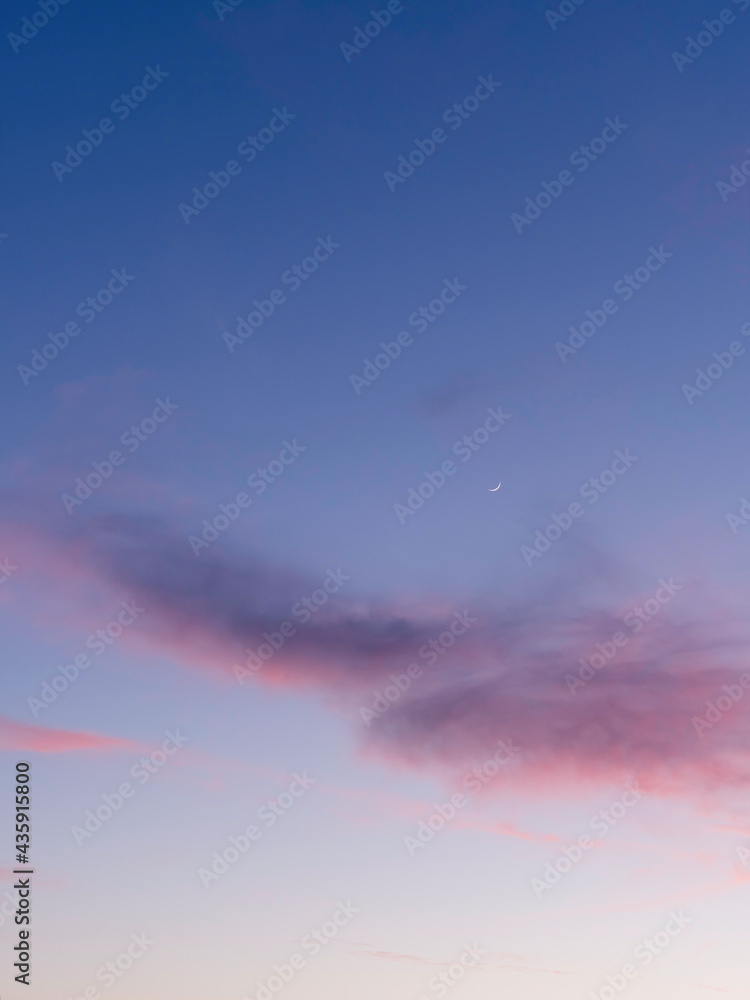 Beautiful sunset with pink clouds on clear blue sky with sickle of the waxing moon. Colorful panorama of heavens. Peaceful atmosphere of evening. Dusk time of a day. Beautiful sunset with pink clouds on clear blue sky with sickle of the waxing moon. Colorful panorama of heavens. Peaceful atmosphere of evening. Dusk time of a day.
