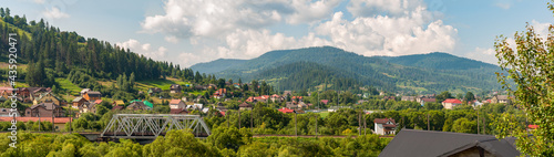 Small village located at bottom small mountains overgrown with green vegetation  tall coniferous and deciduous trees. Nature Ukraine