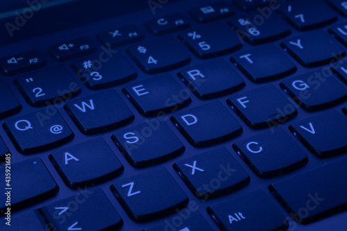 QWERTY Keys of a laptop computer keyboard illuminated with uv ultraviolet purple light