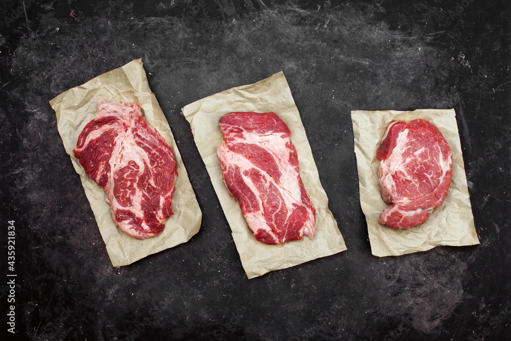 Raw Marbled Loin Beef Steaks On Brown Paper. Sirloin Beef Steaks, Overhead View. Three Raw Striploin Steaks from Marbled Beef on Black Background, Top View.
