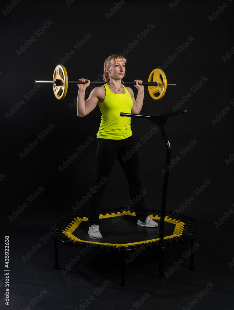 Fototapeta premium Girl on a fitness trampoline on a black background in a yellow t-shirt trampoline energy active activity caucasian movement, muscular club. Fly white motion, physical muscle instructor enjoy