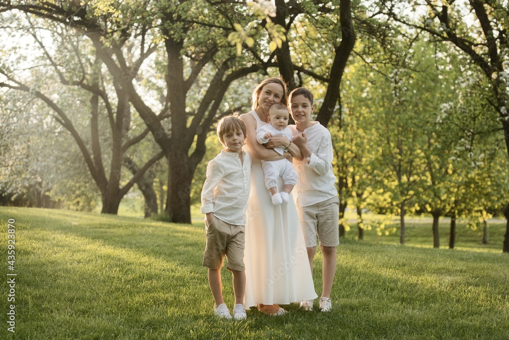 Mother and three children hugging. Happy family sitting outdoor: woman and two brother kids boys and cute little toddler boy Mother and three children hugging. Happy family sitting outdoor: woman and two brother kids boys and cute little toddler boy