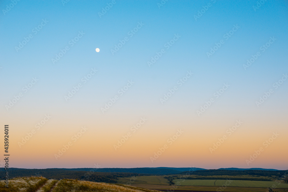 Sunset and moon over the field and forest.