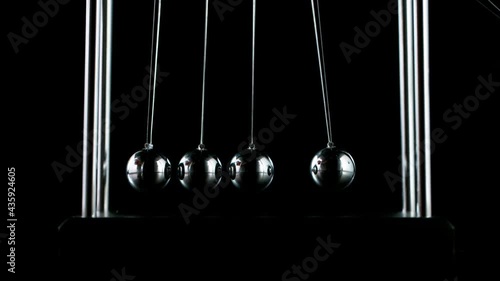 Slow motion shot of swinging metal balls on black background. Newton's cradle.