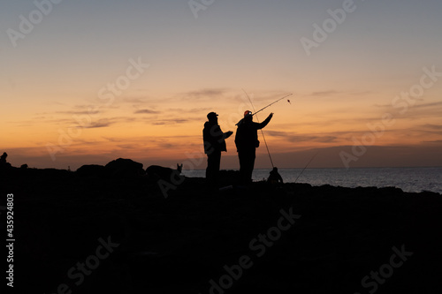 Silhouettes of two fishermen getting ready at sunset to fishing