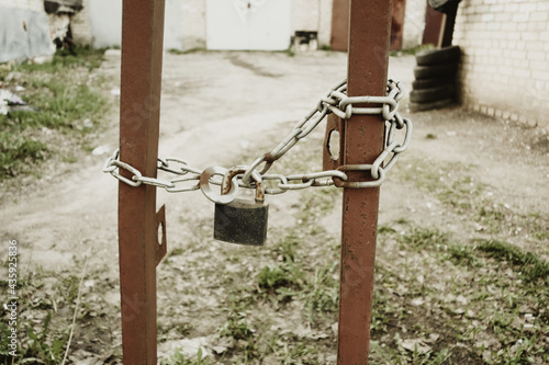 Fotografija An old rusty brown gate with a padlock on a chain closes the passage to the private territory