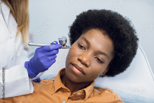 Non-injectable mesotherapy, skin revitalizaion, oxygen peeling concept. Closeup portrait of lovely african young woman getting oxygen skin care therapy in a beauty salon