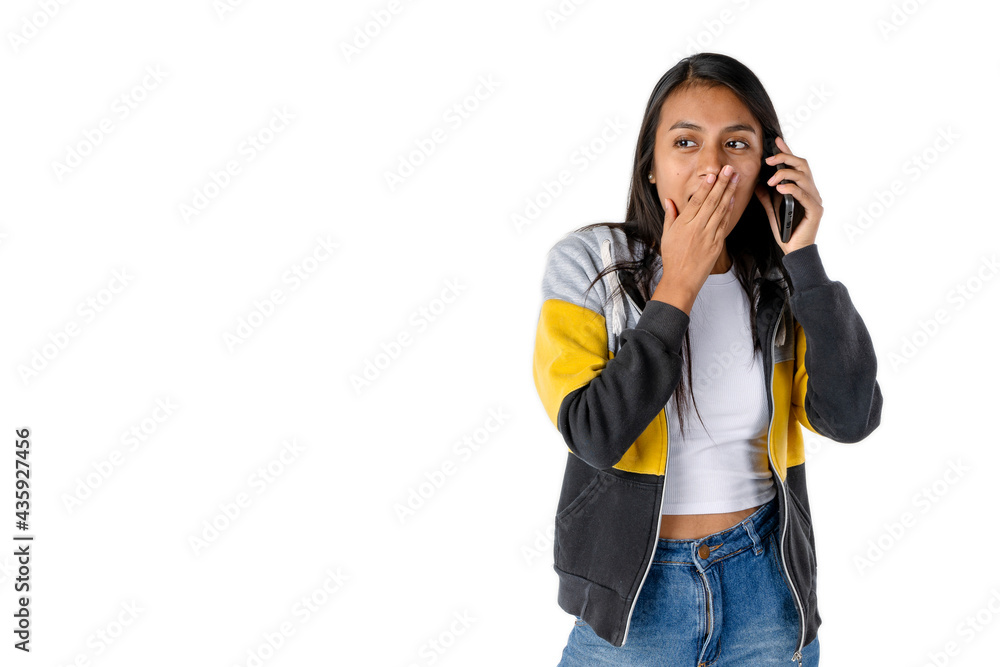 Attractive Latin woman with surprised expression and her hand covering her mouth while listening to a message or to her interlocutor on a cell phone on white background. Technology and communications Attractive Latin woman with surprised expression and her hand covering her mouth while listening to a message or to her interlocutor on a cell phone on white background. Technology and communications