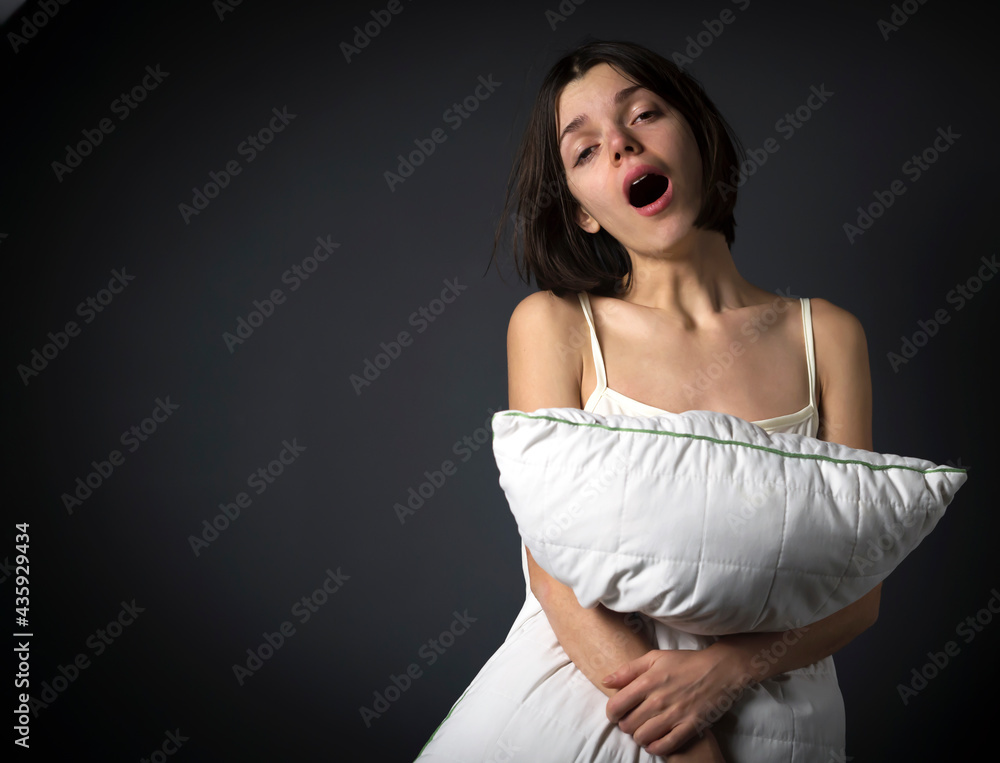 Fototapeta premium Young cute girl just woke up in her cozy bed at home in the morning. A smiling woman hugs the pillow lazily procrastinates and does not want to go to work, prefers to sleep longer.