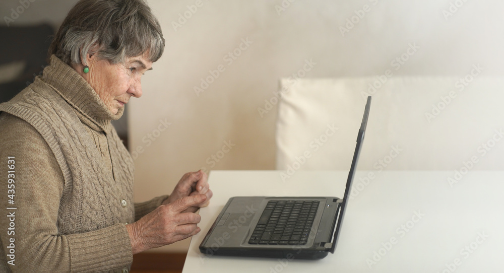 Old woman wearing casual clothes such as knitted sweater, spending free time at cozy home, sitting, resting using pc, typing message and searching, reading news online. Old woman wearing casual clothes such as knitted sweater, spending free time at cozy home, sitting, resting using pc, typing message and searching, reading news online.