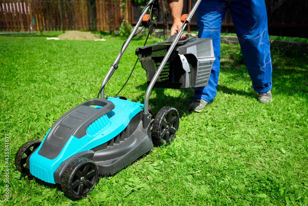 Fototapeta premium Male worker on the street working on mowing the lawn with the help of a modern lawn mower near a country house