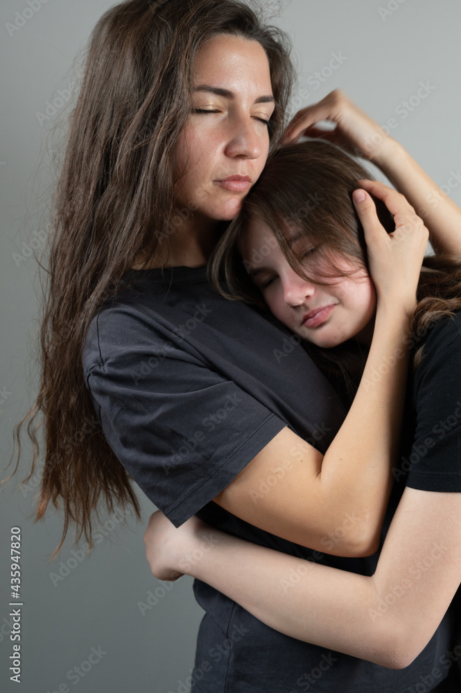 Close up of mother hugging teenage girl with care and love. Problems awkward age concept Close up of mother hugging teenage girl with care and love. Problems awkward age concept