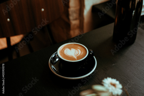 Cup of cappuccino coffee on black wooden table at cofffe shop. Lights and shadows, dark food drink photography concept. Lovely, calm, tasty, atmospheric moody shot. Close up photo