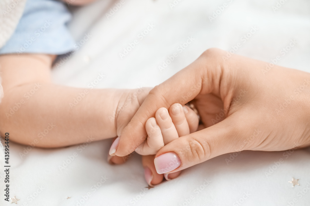 Hand of mother and cute little baby on bed, closeup Hand of mother and cute little baby on bed, closeup