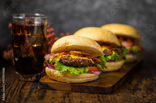 Selective focus on hamburgers with beef burgers, fried onions, spinach, ketchup, pepper and cheese served on a wooden board with soft drink.