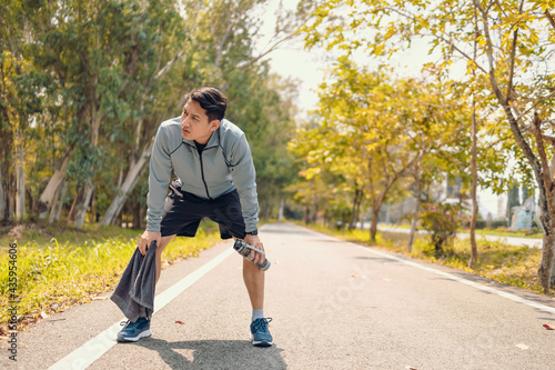 a tired young man resting and breathing holding a bottle of drinking water and towel on the road in the park morning. photo