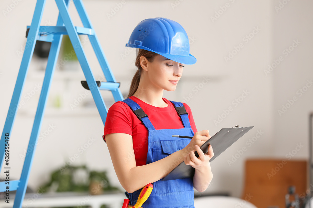 Fototapeta premium Beautiful female electrician writing in clipboard in room