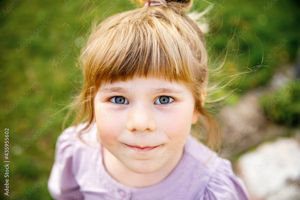 Portrait of happy smiling toddler girl outdoors. Little child with blond hairs looking and smiling at the camera. Happy healthy child enjoy outdoor activity and playing. Portrait of happy smiling toddler girl outdoors. Little child with blond hairs looking and smiling at the camera. Happy healthy child enjoy outdoor activity and playing.