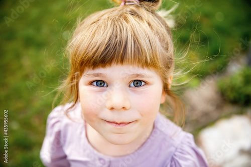 Portrait of happy smiling toddler girl outdoors. Little child with blond hairs looking and smiling at the camera. Happy healthy child enjoy outdoor activity and playing.