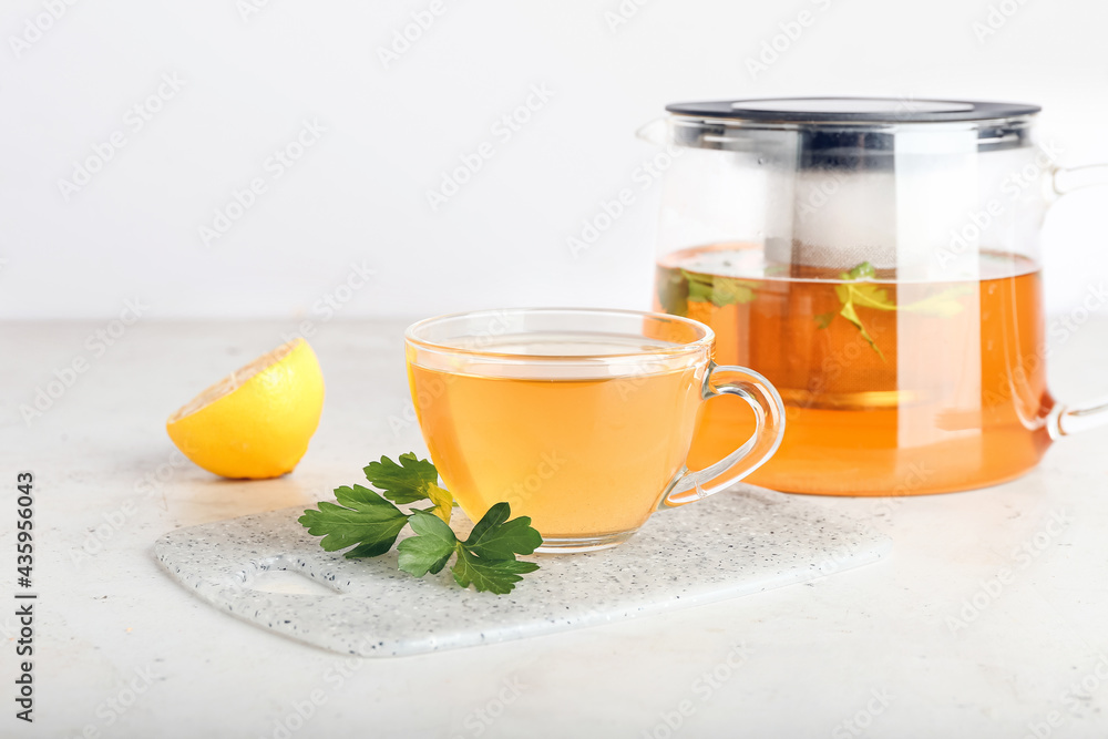 Teapot and cup of hot tea, parsley and lemon on light background Teapot and cup of hot tea, parsley and lemon on light background