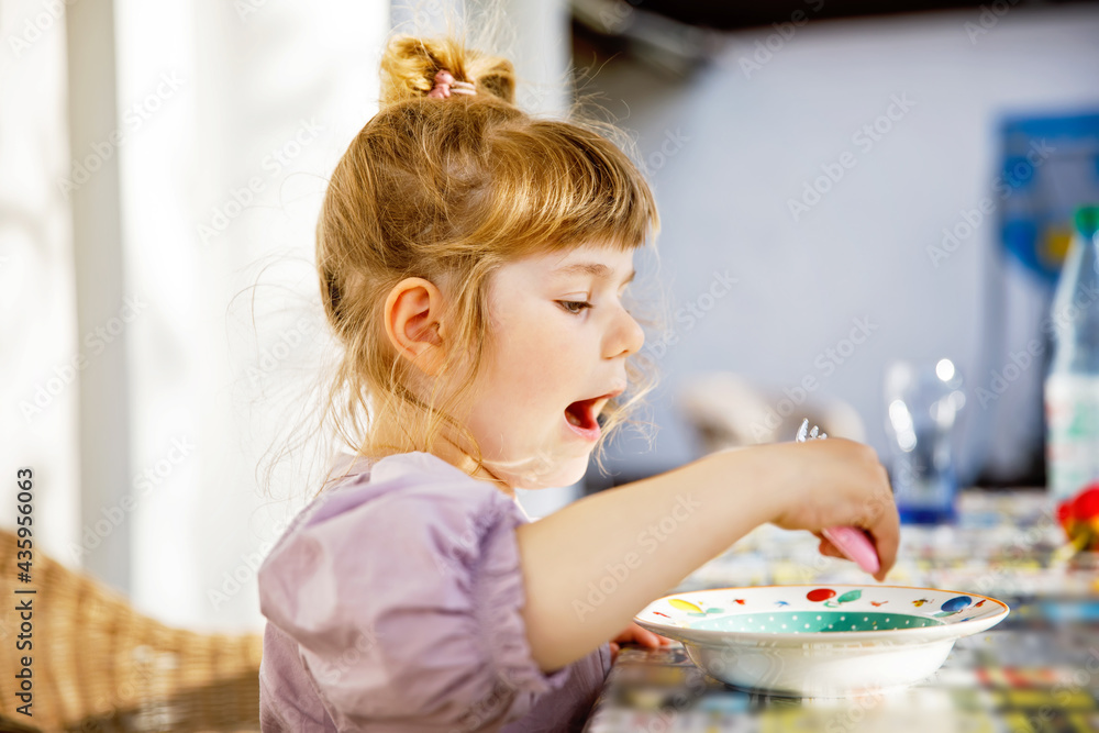 Portrait of happy smiling toddler girl eating pasta on domestic terrace outdoors. Little child with blond hairs enjoy healthy fresh prepared lunch. Happy healthy child and food for children.