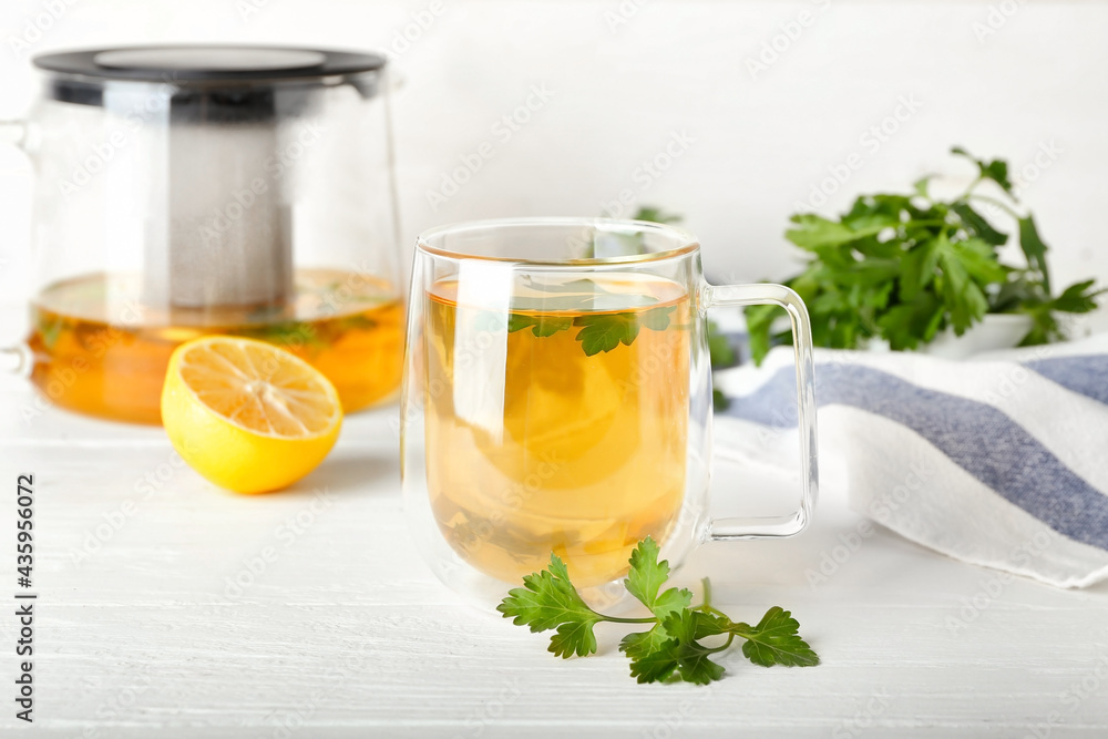 Cup of hot tea, parsley and lemon on light wooden background
